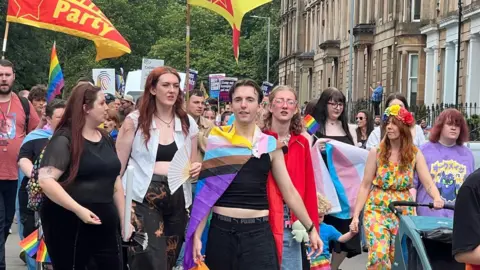 Pride marchers in Glasgow carrying flags and wearing colourful clothes  