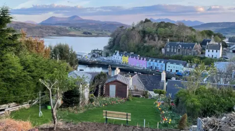 Helen Wilson A garden bench among tulips overlooking the beautiful view of the colourful houses at the harbour and the distant red and black Cuillins.