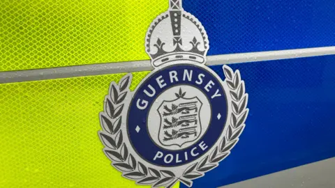 BBC A close up of the Guernsey police logo. It includes three lions and a crown. 
