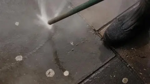 A street cleaner hoses chewing gum from a pavement 