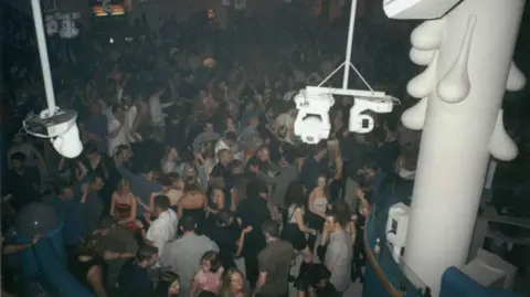 ESP Magazine A crowd of people dancing in a nightclub flanked by lights.