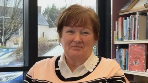 Frances has brown hair and is smiling at the camera. She is wearing a striped jumper with a white collar. 