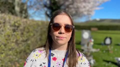 A woman wearing a knitted jumper with flowers and sunglasses.