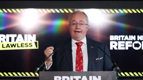 Getty Images A man in a suit and tie in front a screen saying "Britain is Lawless"