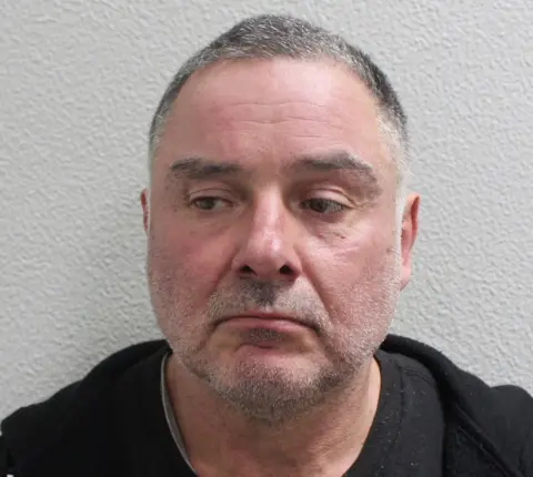 Metropolitan Police Custody image of Thomas McKenna, wearing a dark top, photographed against a plain wall.