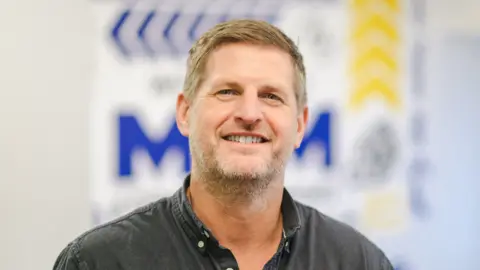 Jamie Akrill/MKM Building Supplies Andy Pickup wearing a black shirt, with a button-down collar.