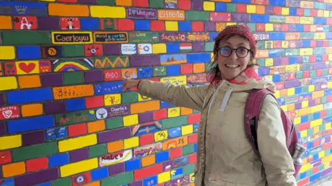 Dan Petley Fraisia in front of a mural, pointing towards it and smiling to camera