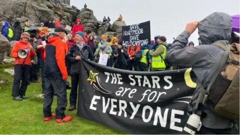 Campaigners connected  Dartmoor with a banner saying The Stars are for Everyone and different  saying Save Dartmoor Wild Camping with a backdrop of a rocky outcrop emblematic  of Dartmoor landscape.