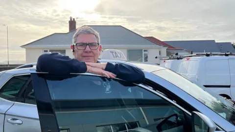 Ian Vaudin leaning on the door of his taxi