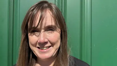 Cathy O'Neill  wearing a black top standing in front of a green door. 