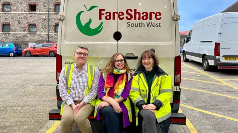 Julian Mines, Helen Godwin and Josie Forsyth sitting on the back of a white van bearing the logo 'FareShare South West'
