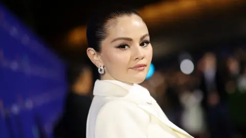 Getty Images Selena Gomez with her dark hair swept up, wearing a cream blazer, at the Palm Springs International Film Awards earlier this month