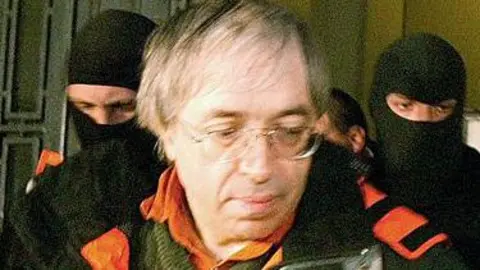 Getty Images A picture of Gregorian Bivolaru - wearing a green jumper and an orange and black coat, with long, thin white hair - being arrested in Romania in 2004