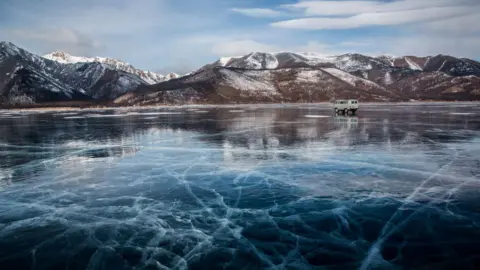 Getty Images Frozen lake with snow covered hills in the background. A van is parked on the ice.