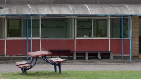 BBC/ Gemma Laiser Um banco de piquenique torto em um pedaço de grama do lado de fora de um dos prédios da Patchway Community School, que se acredita ter sido construído na década de 1950.