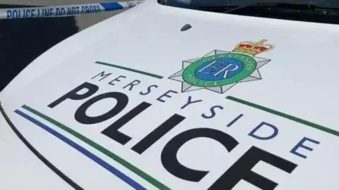 PA Media Stock shot of the bonnet of a Merseyside Police van, which is white. The text 'MERSEYSIDE POLICE' is seen on the front in black and blue lettering.