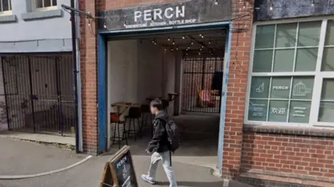 Google A man walks past the Perch pub on Garden Street in Sheffield city centre, which has white steel windows and a brick façade, with an A-board sign outside.