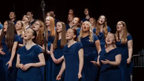 A group of teenage girls wearing dark blue dresses singing in a choir