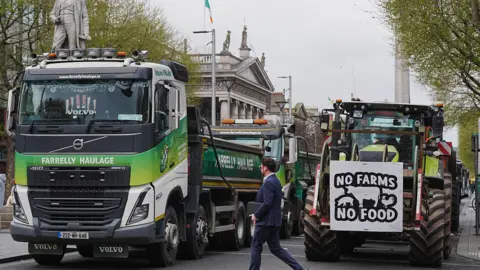 Brian Lawless/PA Wire A long queue of tractors on a street. A poster says no farms, no food.