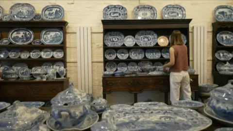 A collection of ceramic plates with blue patterns on display on shelves and tables in a large room