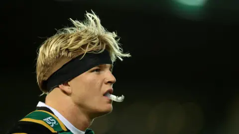 Reuters/Andrew Boyers Henry Pollock wearing a green, gold and black shirt of Northampton Saints, and a black headband and a mouth guard. He has blonde hair.  