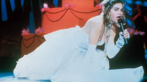 Getty Images Madonna in a wedding dress crouched on the stage and singing into a microphone