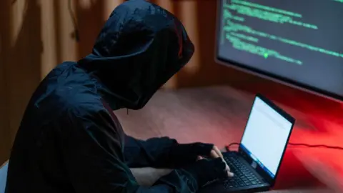 A man in dark clothing posing as a cyber-criminal
