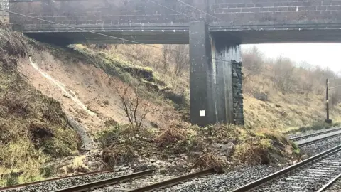 A landslip across the railway line with a bridge in the background