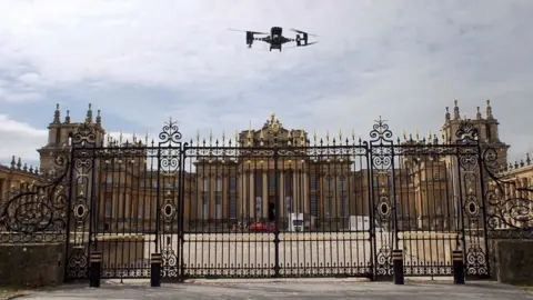 Thames Valley Police Drone hovering just above the black and gold entrance gates with Blenheim Palace in the background