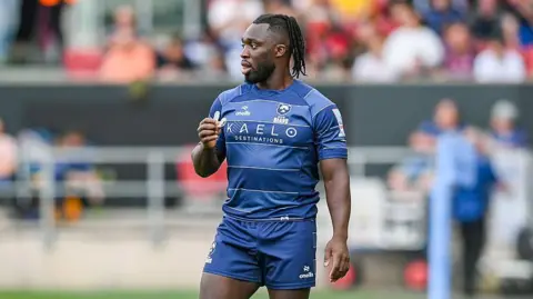 Gabriel Ibitoye standing on the pitch holding his mouth guard in his left hand during Bristol's game against Saracens 