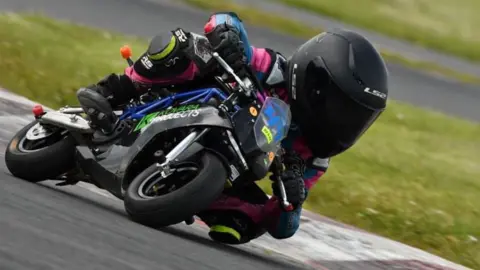 David Baldwin Photography Seven-year-old Nellie racing on her motorcycle on a racing track. She is wearing a black helmet and pink leathers.