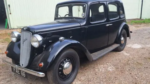 A refurbished, black 1938 Austin 10 Cambridge parked outside a garage.