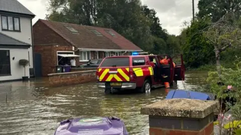 Woolgrove Road in Hitchin, Hertfordshire, showing flooded houses and a Fire and Rescue vehicle in the middle of a flooded road