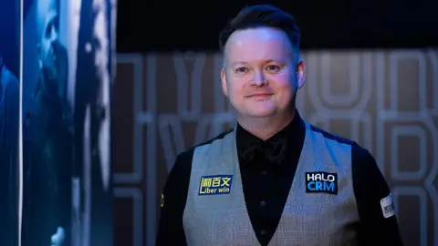A smiling Shaun Murphy in black shirt and bow tie, and grey waistcoat