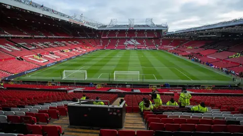 Getty Images A general view of the Old Trafford ground during the Premier League match between Manchester United and Tottenham Hotspur at on 7 February 2026. The neatly cut turf is surrounded by the stands with the team's name depicted in white on the unoccupied seats.