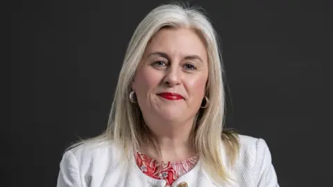 A woman with light hair in a white jacket.