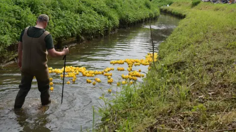 A man guiding rubber ducks down a beck in Wilberfoss