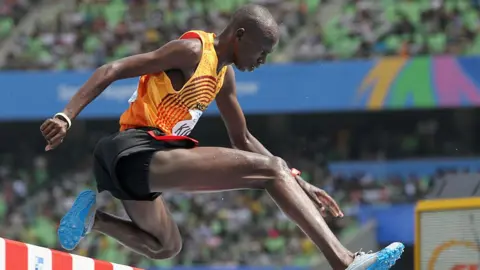 A side view of Benjamin Kiplagat leaping over a hurdle.