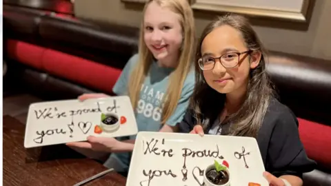 Family photo Two girls holding up plates with the words "We're proud of you" written in chocolate sauce.