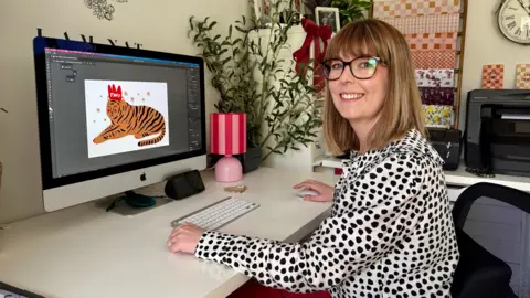 BBC / Becki Bowden Natalie Ramsell-Lee. She is sitting at a desk, working on a design on a computer screen in front of her. 