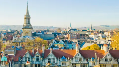 A skyline view of the city of Oxford, with historic looking buildings blending in with the greenery from trees .
