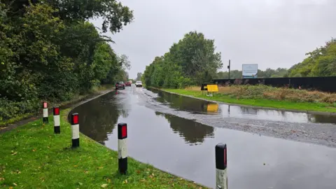 Wendy Windblows Standing water on the bend of a road in Brampton with approaching cars in the distance