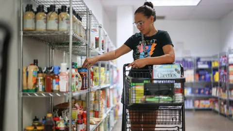 Getty Images Woman rolls shopping cart down food pantry aisle
