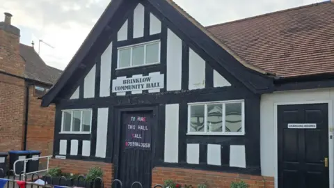A small black and white entrance to a tudor community hall in a village. A sign above the door reads "Brinklow Community Hall".