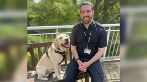 Wiltshire Police PC Croft sitting on a bench beside a Labrador 