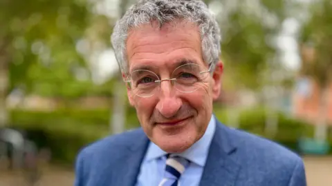 Head and shoulders image of Peter Prinsley MP. He is wearing a blue jacket, shirt and striped tie.