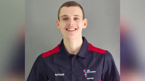 A teenage boy, wearing a GB deaf swimming polo shirt, smiles at the camera.