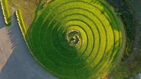 Mike Bolam An aerial view of a landscape artwork on a swirling hilltop with rocks on top
