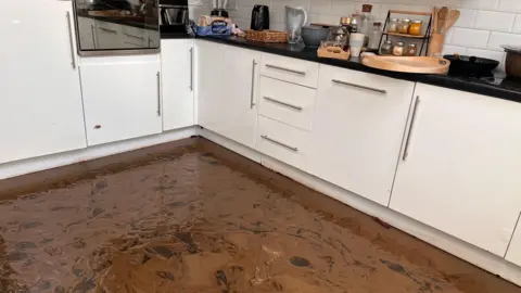 The floor of Mehdi Mozadeh's kitchen in Park Avenue, Dundonald was covered in flood water and brown mud.  The kitchen has white cupboards and there is kitchen equipment on the worktops.