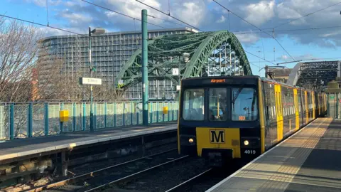 BBC A black and yellow old Metro train approaches Sunderland's St Peter's station. The green arched Wearmouth Bridge can be seen in the background, as well as the tall grey Echo Building.